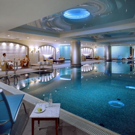 Regent Warsaw Hotel Facilities photo The photo shows a luxurious indoor swimming pool area. The pool has a sparkling blue water surface, and its surroundings are designed with sleek, contemporary architecture. The lighting is soft, with blue accents illuminating the space. On one side, 