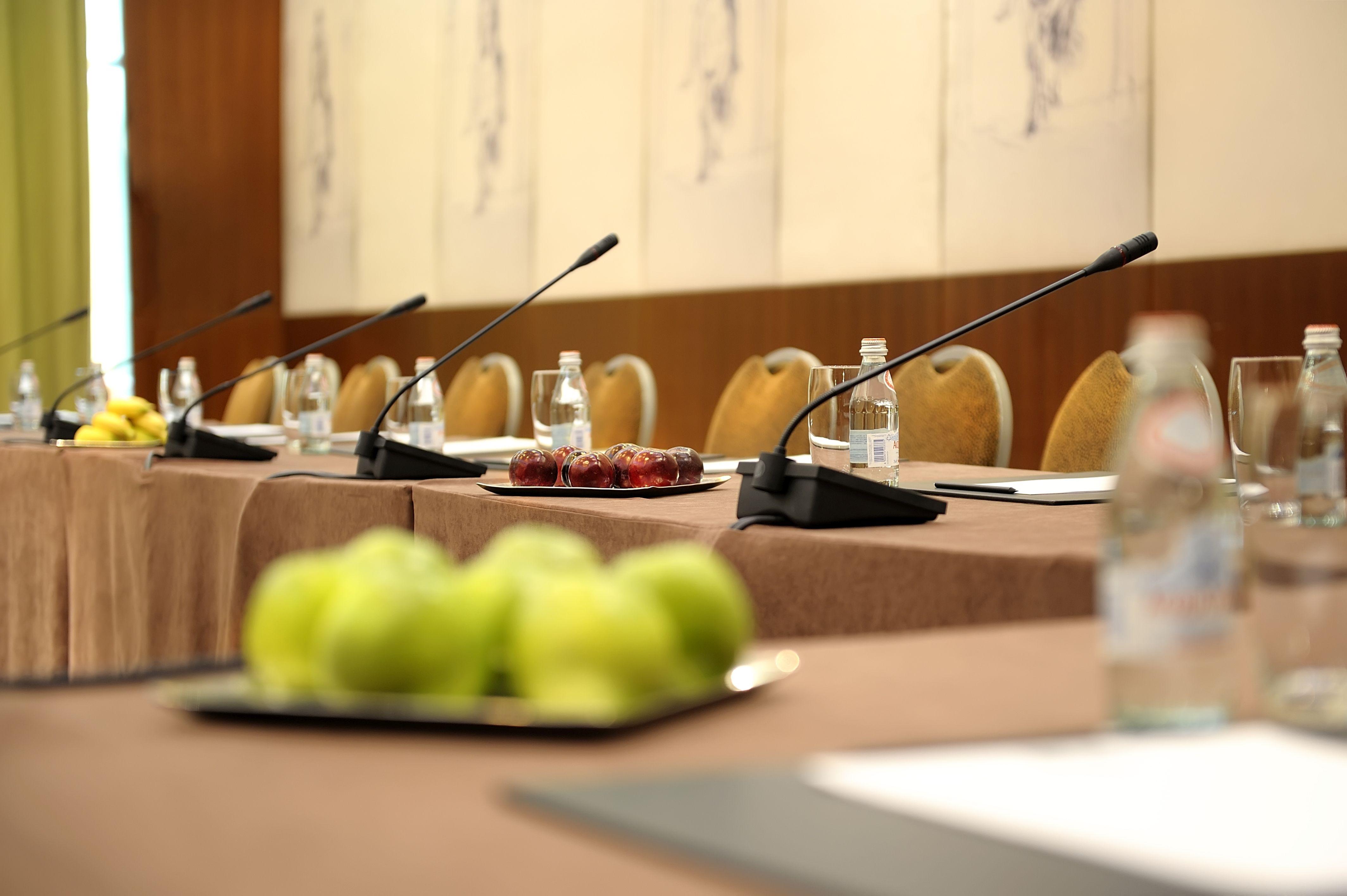 Regent Warsaw Hotel Exterior photo The photo depicts a conference room setup. There are several chairs arranged around a rectangular table covered with a brown tablecloth. Each place at the table has a microphone and a water bottle in front. On the table, there is a plate of dates and