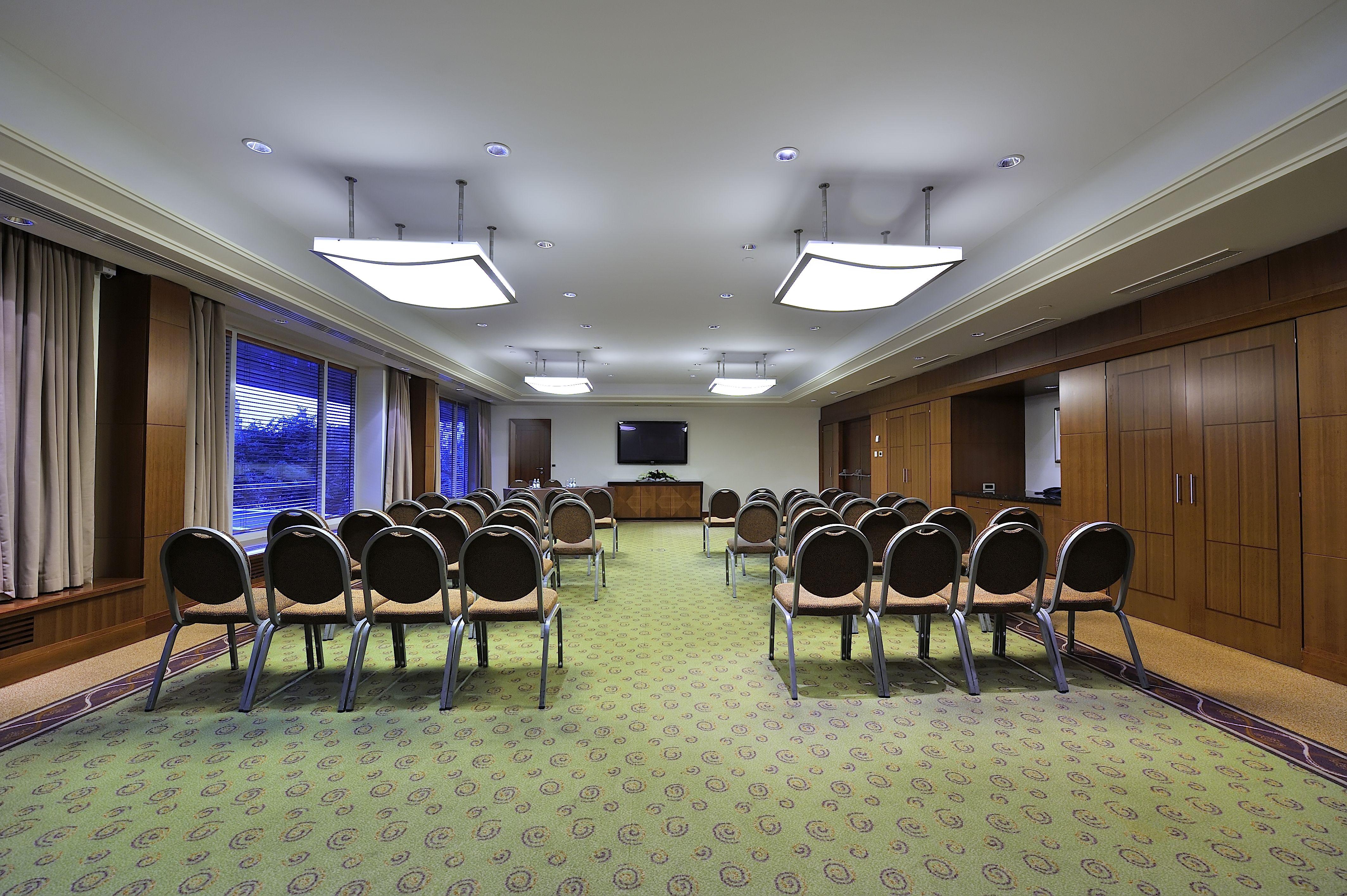 Regent Warsaw Hotel Exterior photo The photo shows a conference room or meeting space. It features several rows of chairs arranged in a semi-circle facing a wall-mounted television. The room has a carpeted floor with a patterned design and is illuminated by rectangular ceiling lights.