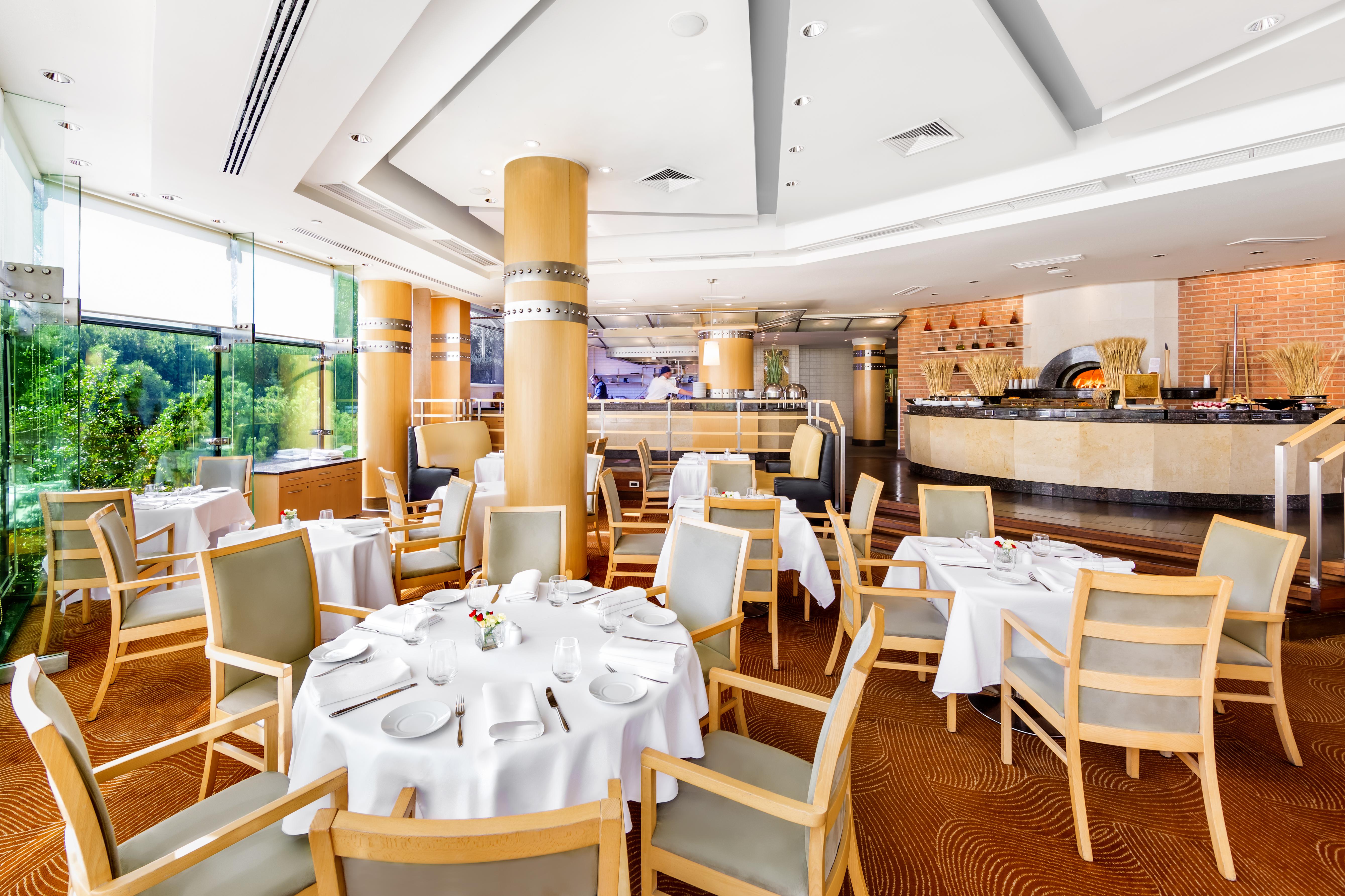Regent Warsaw Hotel Exterior photo The photo shows an elegant dining area within a restaurant. There are multiple round tables covered with white tablecloths, each set with plates and cutlery, indicating a formal dining setup. The chairs are made of light-colored wood with soft cushio