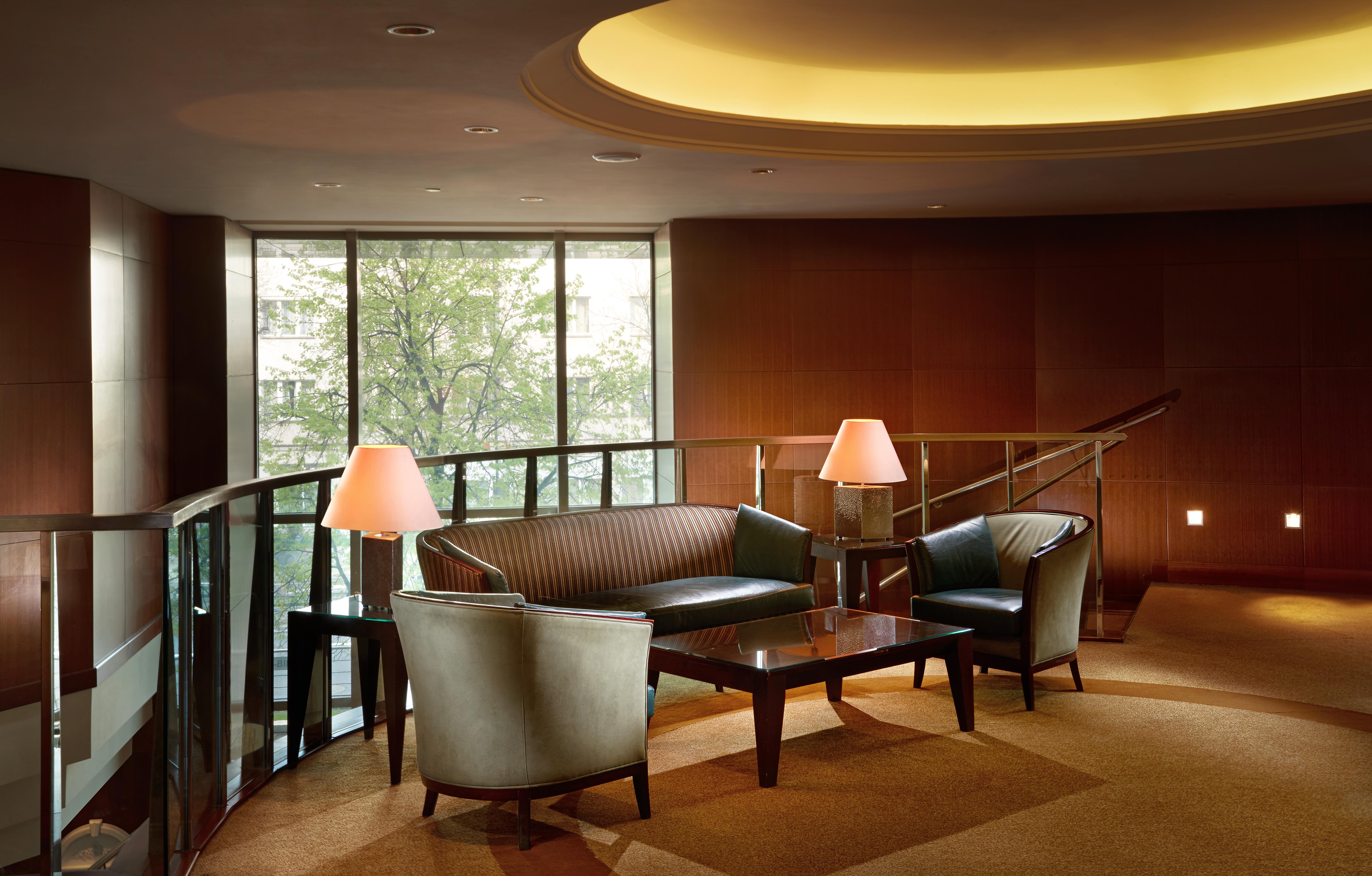 Regent Warsaw Hotel Exterior photo The photo depicts a modern lounge area. It features a curved seating arrangement with a dark, leather couch and two matching armchairs. A sleek coffee table is placed in the center, and there are two lamps providing soft lighting. The space is enhanc