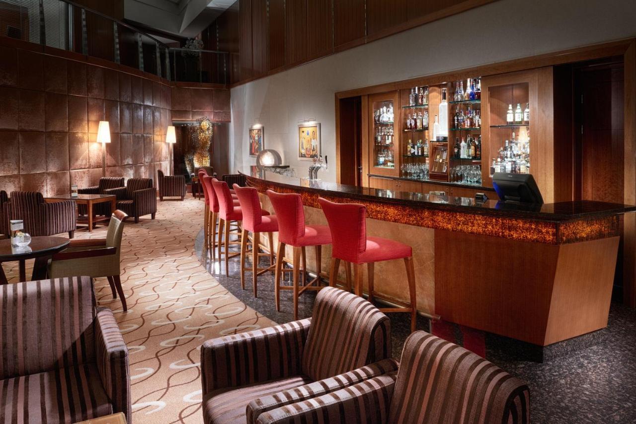 Regent Warsaw Hotel Exterior photo The photo shows a stylish and sophisticated bar interior. There are several tall bar stools with red upholstery positioned along a polished wooden bar counter. Behind the bar, shelves display a variety of bottles and glassware, indicating a well-stoc