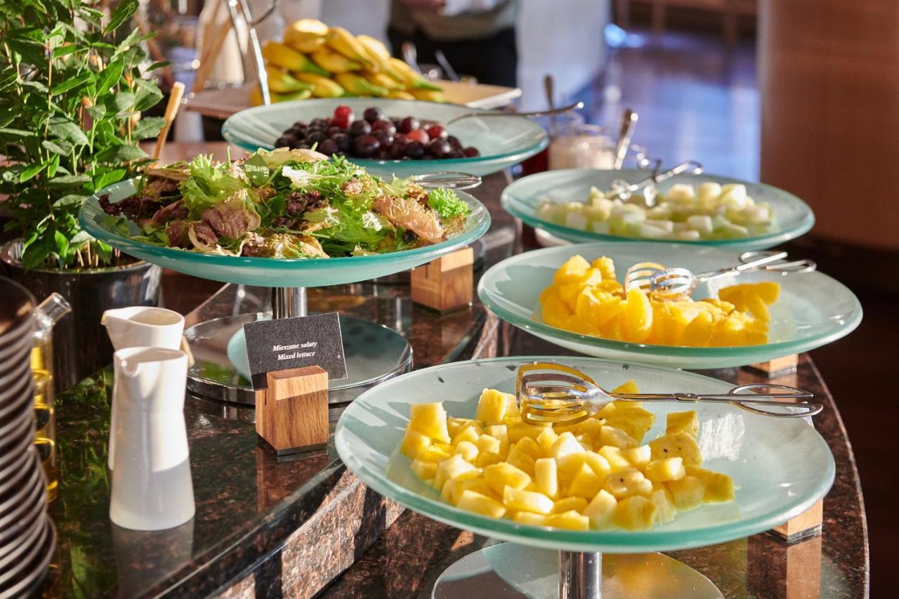 Regent Warsaw Hotel Exterior photo The photo displays a buffet-style setup featuring a variety of food items. There are several glass trays stacked on a countertop, each holding different types of food. 

1. **Fresh Vegetables and Fruit:** One tray appears to have a mix of leafy green