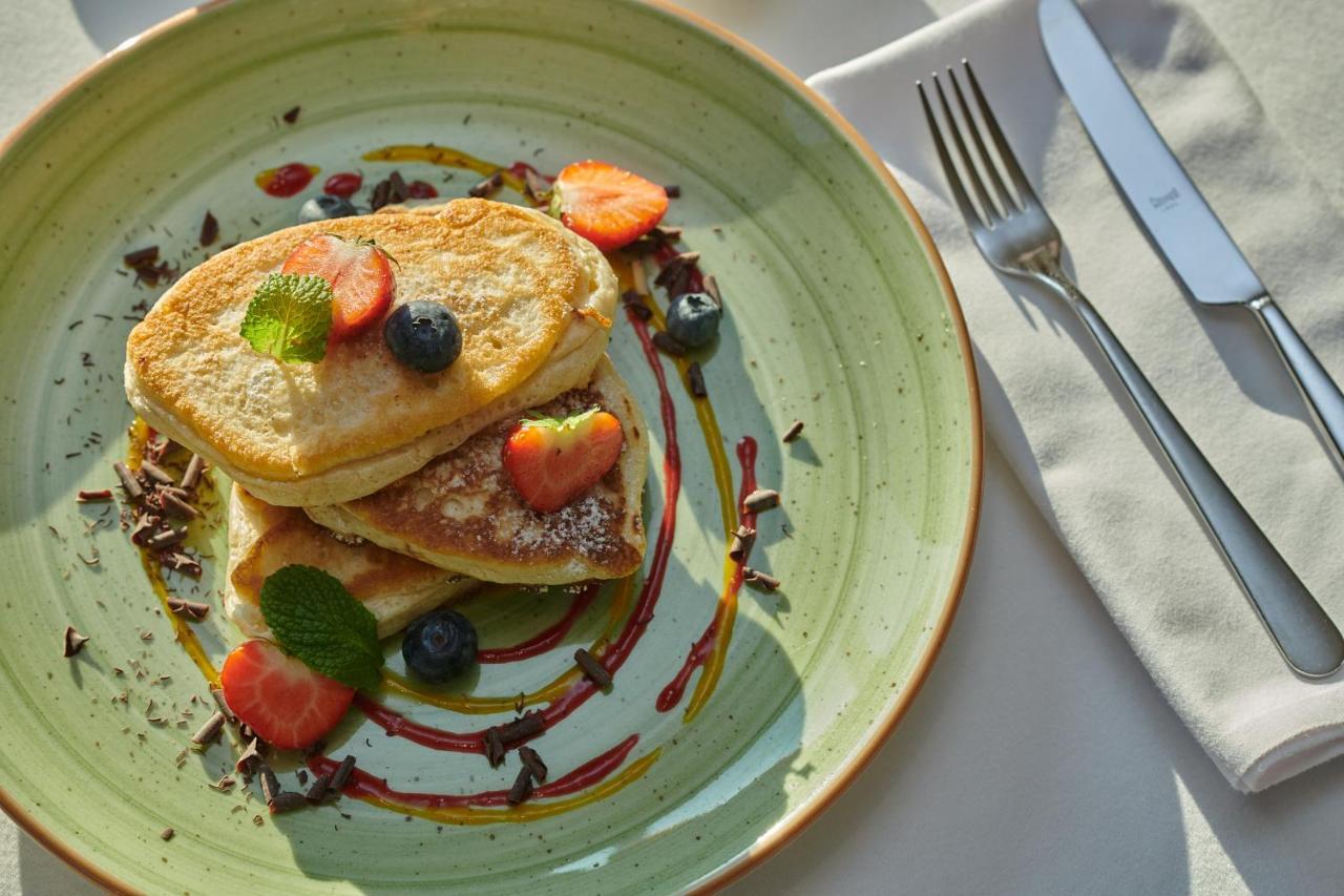 Regent Warsaw Hotel Exterior photo The photo shows a plate of pancakes stacked on top of each other. The pancakes are garnished with fresh strawberries, blueberries, and mint leaves. There are drizzles of syrup and chocolate around the pancakes, adding a colorful touch to the presenta
