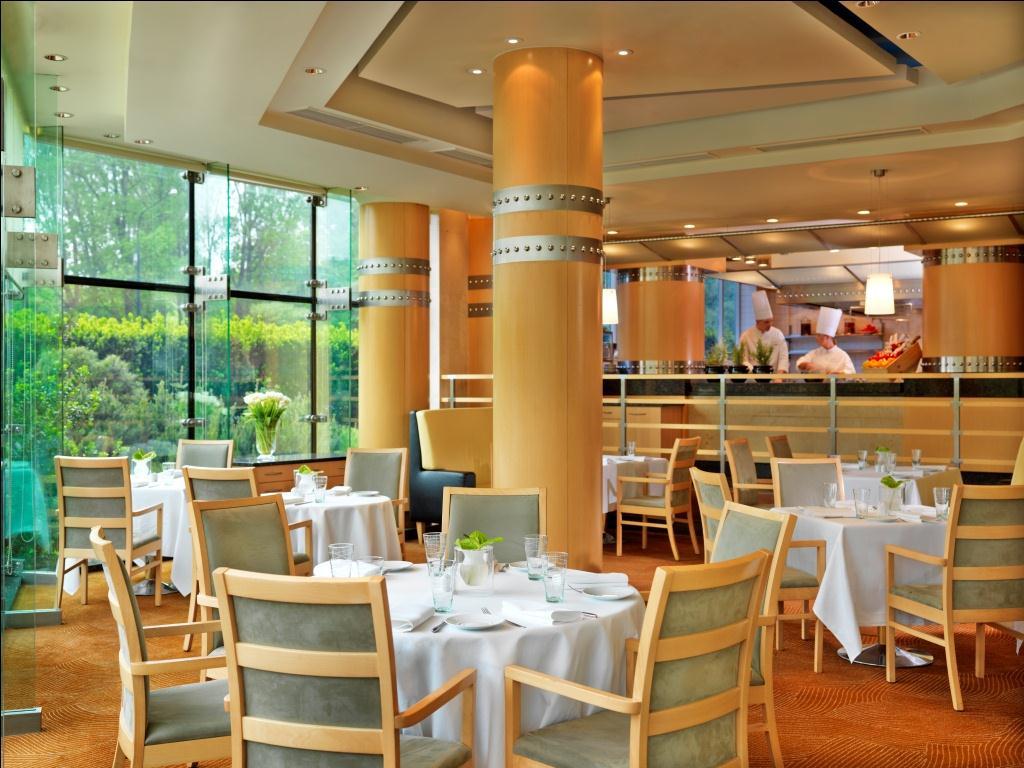 Regent Warsaw Hotel Exterior photo The photo shows an elegant restaurant interior. It features stylish wooden chairs around neatly set tables, which are adorned with white tablecloths and glassware. Large windows allow natural light to fill the space, providing a view of the greenery 