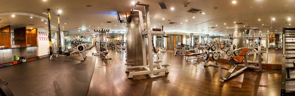 Regent Warsaw Hotel Exterior photo The photo shows an interior gym facility equipped with various exercise machines and weights. The space features a wooden floor and is well-lit, with overhead lighting and large mirrors on the walls. In the foreground, there is a multi-use exercise m