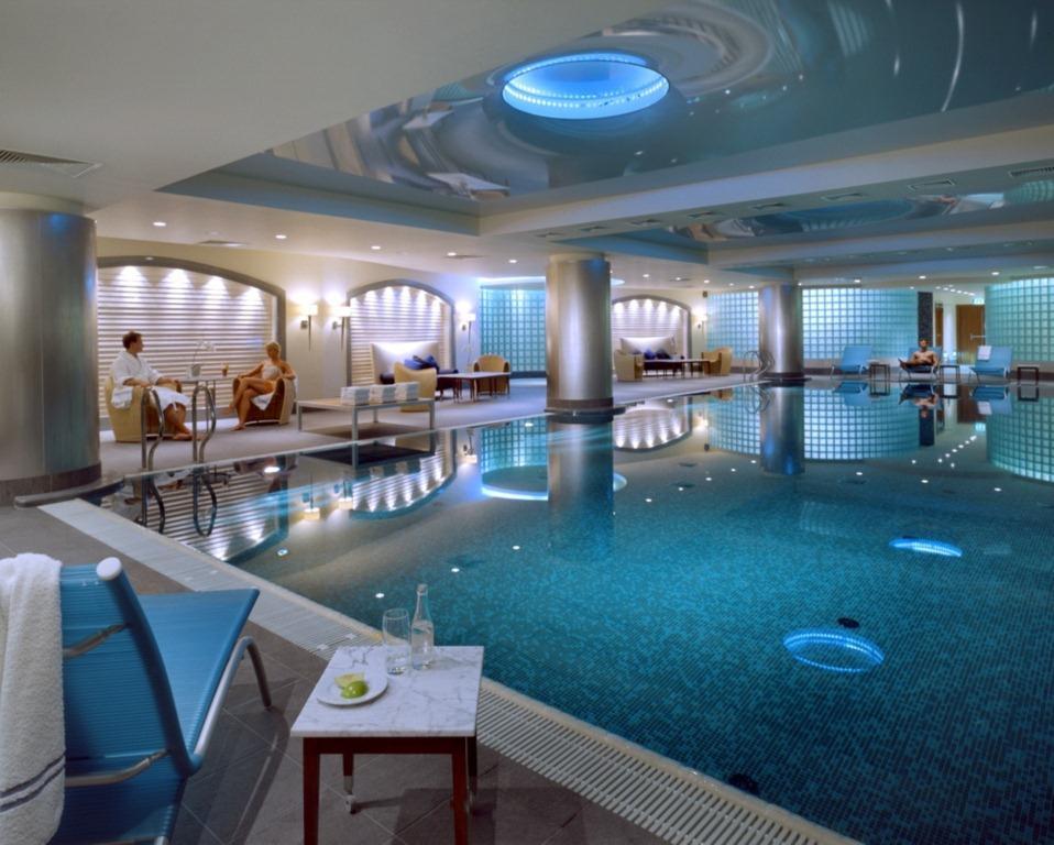 Regent Warsaw Hotel Facilities photo The photo shows a luxurious indoor swimming pool area. The pool has a sparkling blue water surface, and its surroundings are designed with sleek, contemporary architecture. The lighting is soft, with blue accents illuminating the space. On one side, 